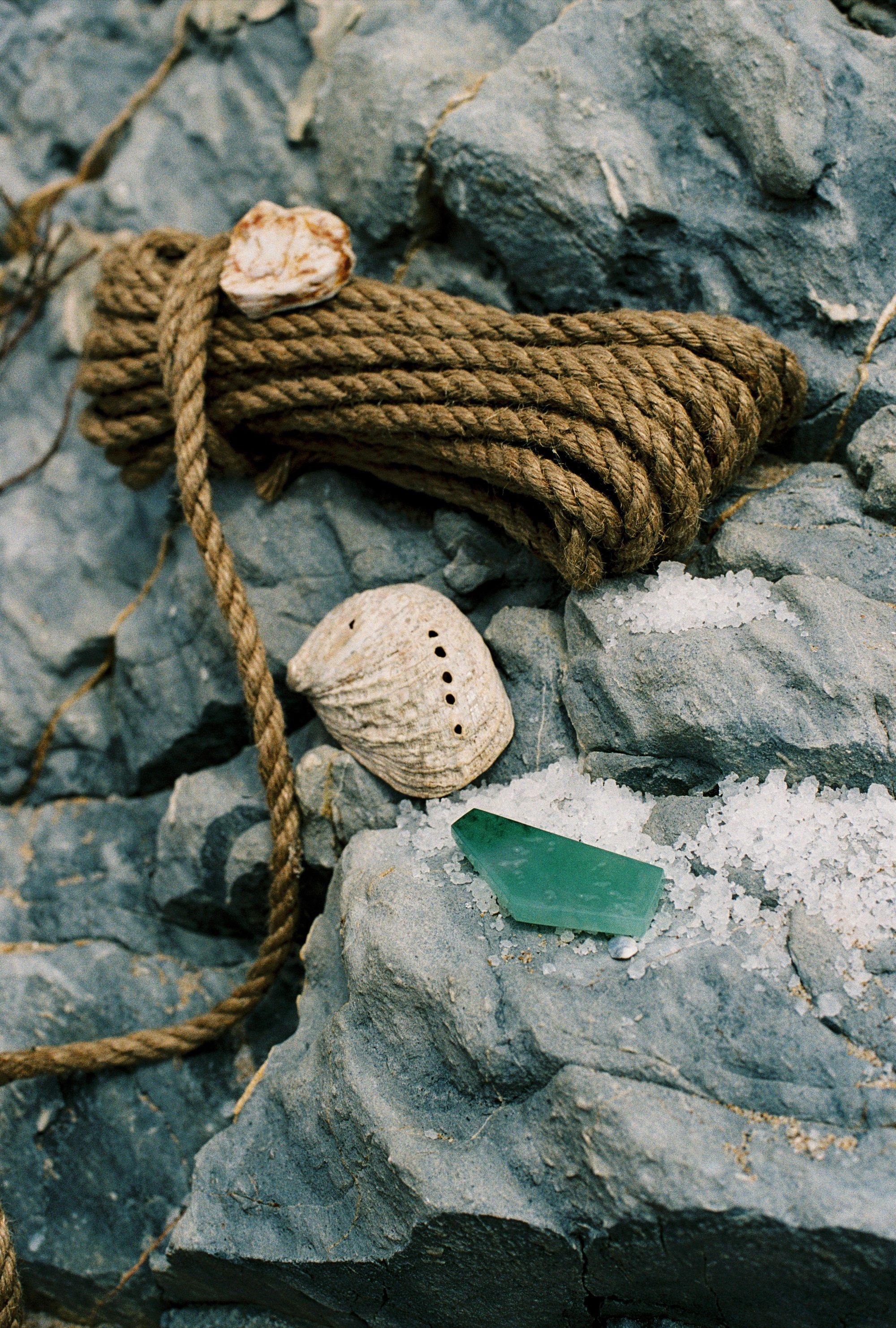 A coil of rope with a shell, sea-glass jadeite and salt on grey rock