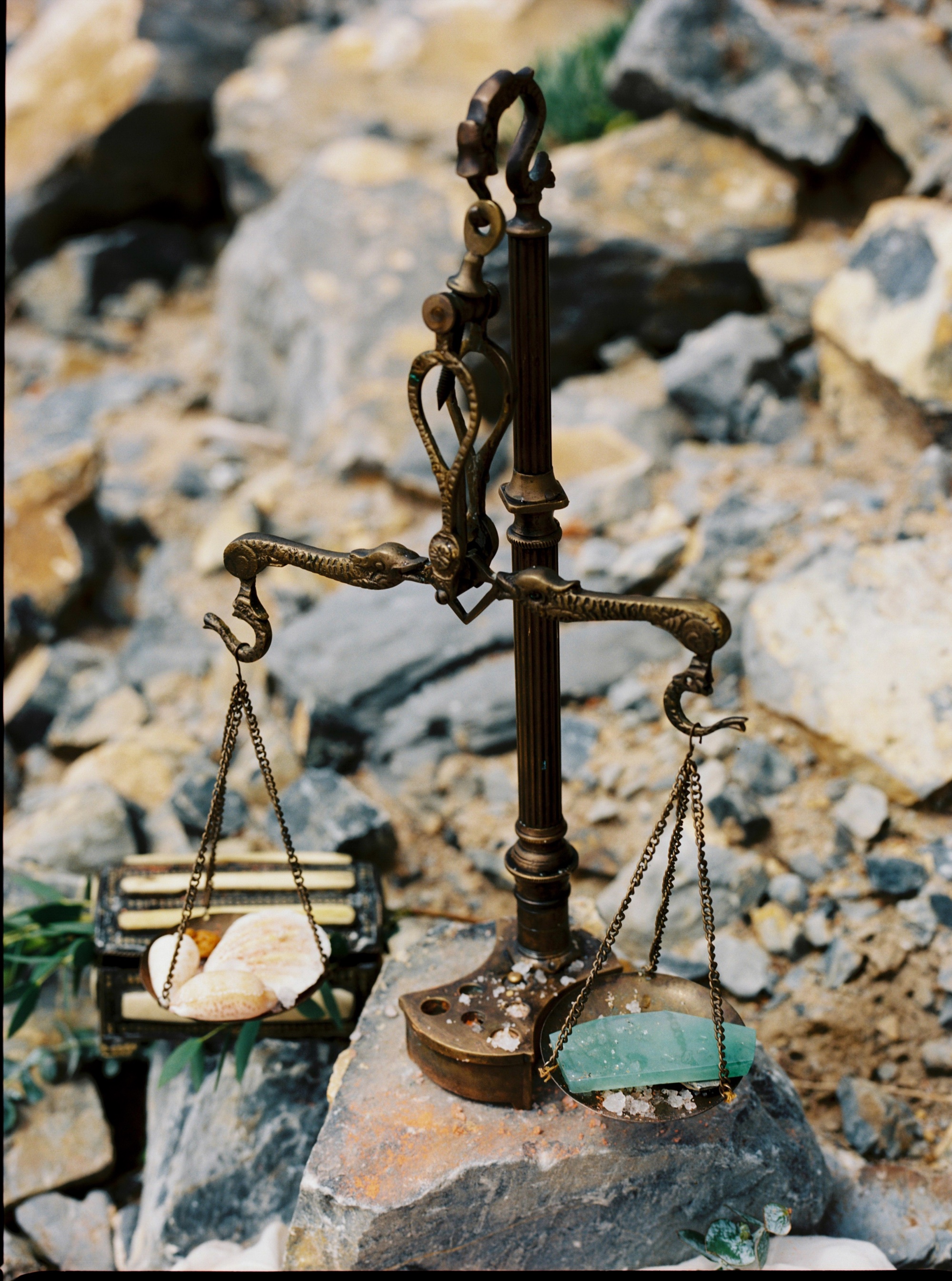 A brass balance scale weighing a piece of jadeite against a stone, set on rocks