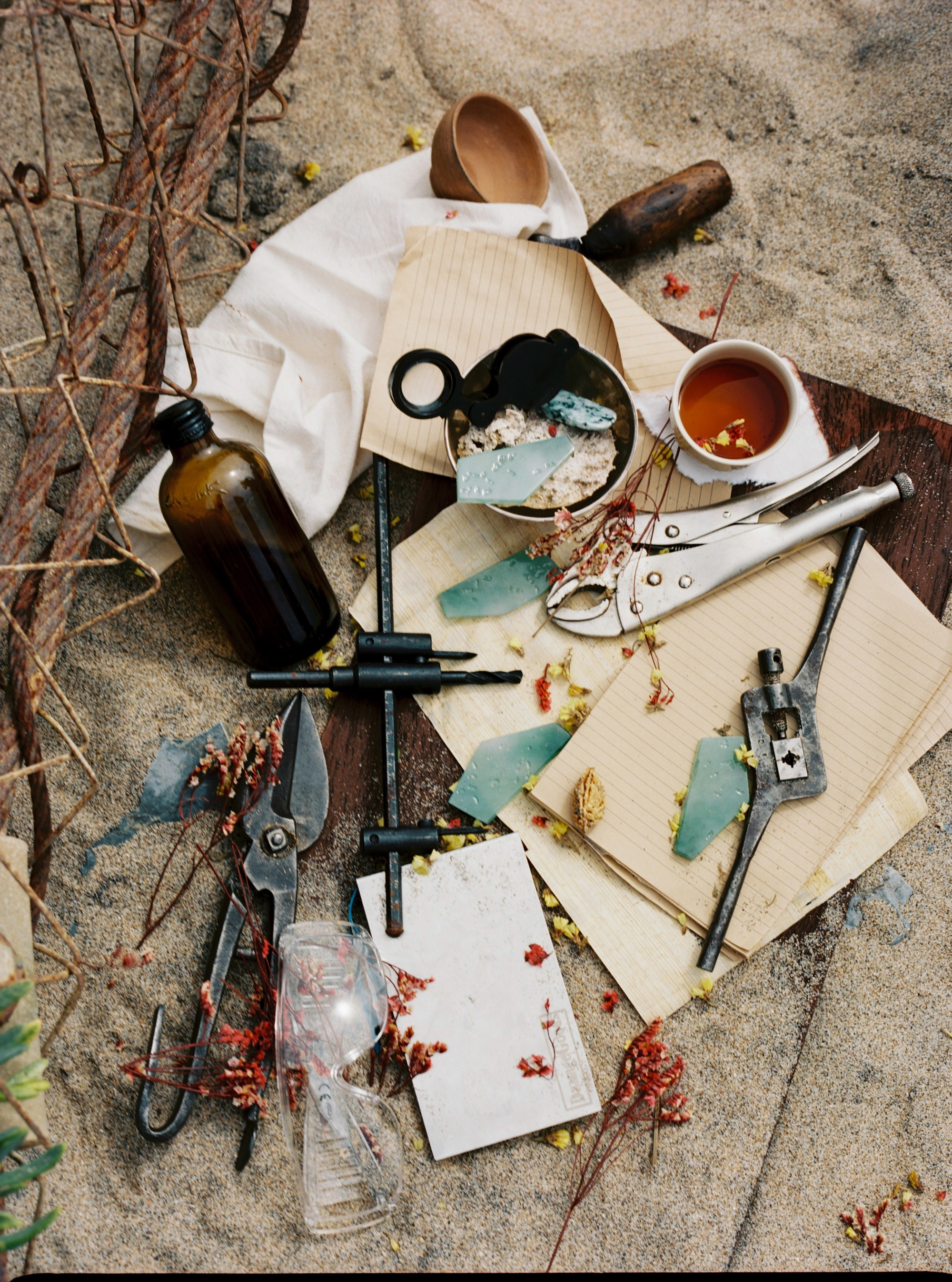 A still life with a bottle, papers, jadeite and instruments laid out on sand