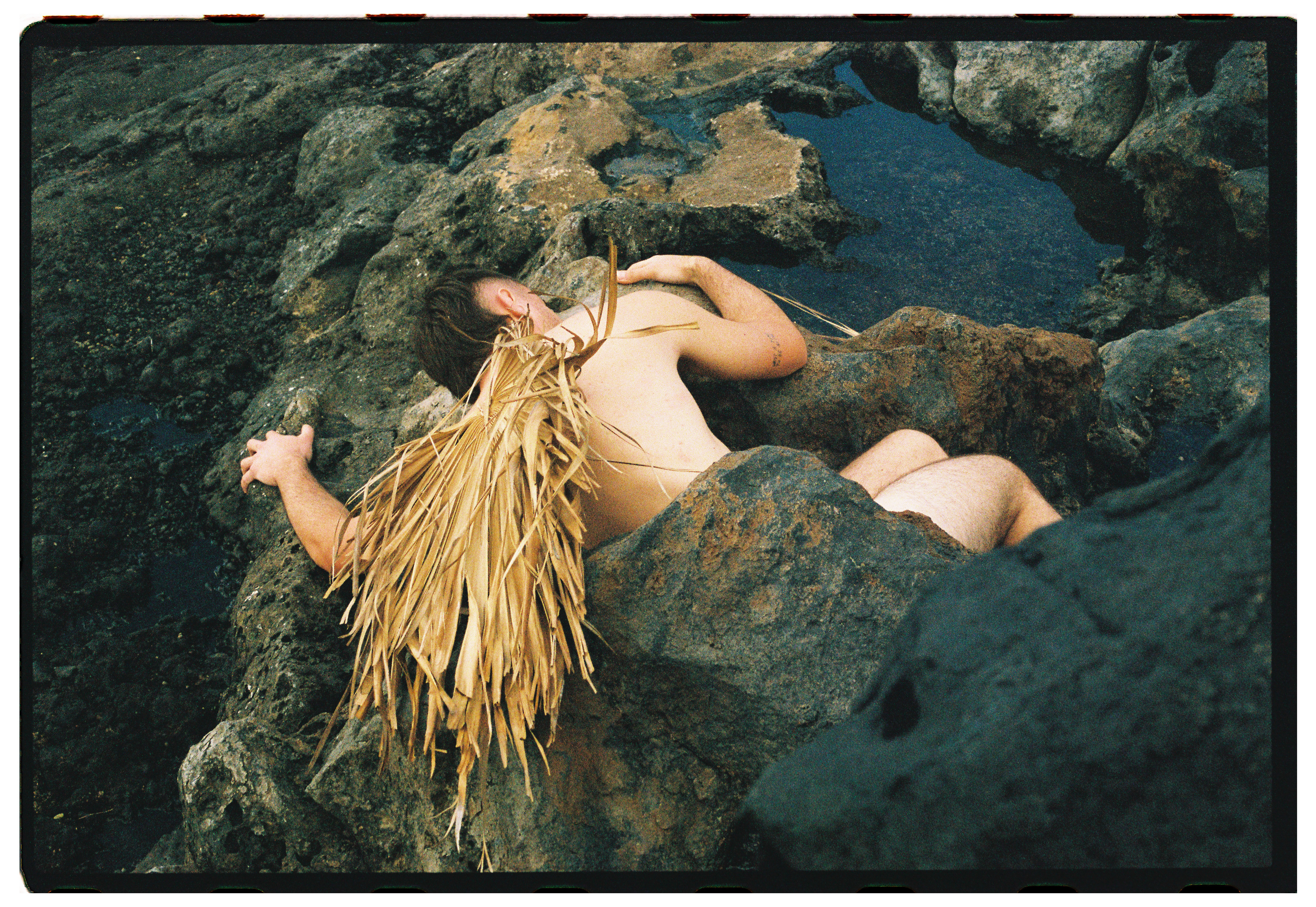 A figure draped over volcanic rock in Lanzarote, raffia across the body